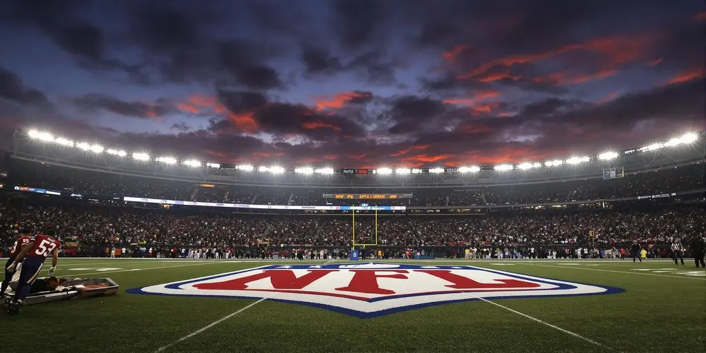 Packed football stadium under lights with NFL logo field