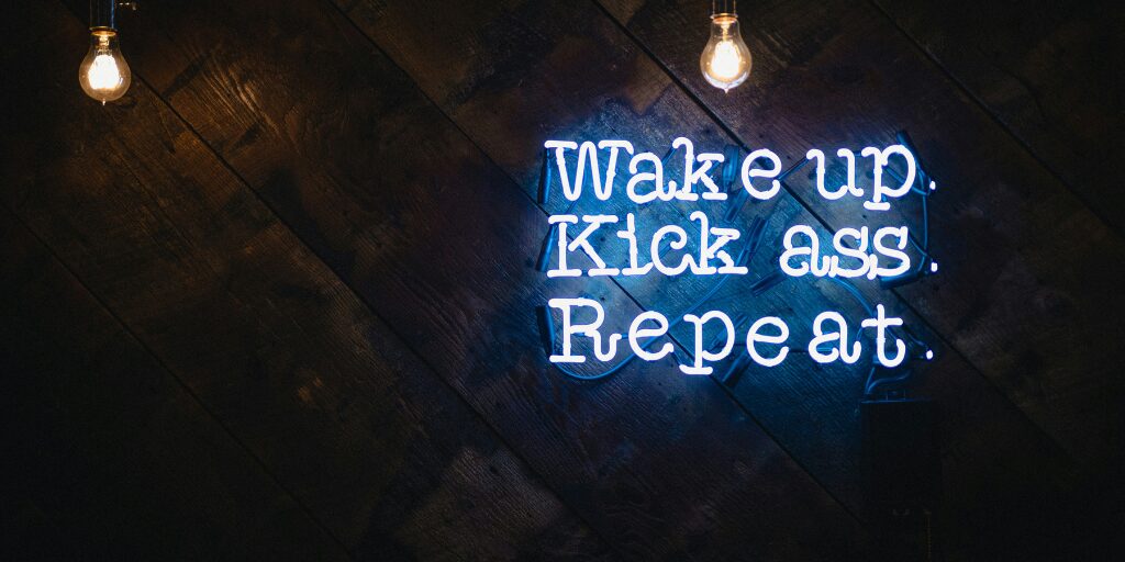 Neon sign on a dark wooden wall displaying a motivational message with two exposed light bulbs hanging above.