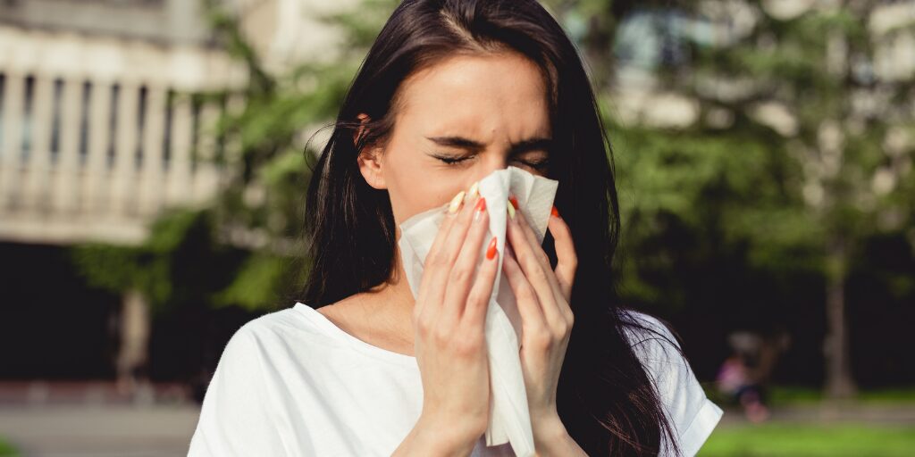 Woman outdoors blowing nose into tissue