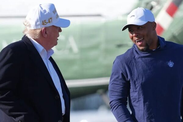 President Donald Trump and football player Saquon Barkley, wearing casual clothing and caps, talking and smiling outdoors.