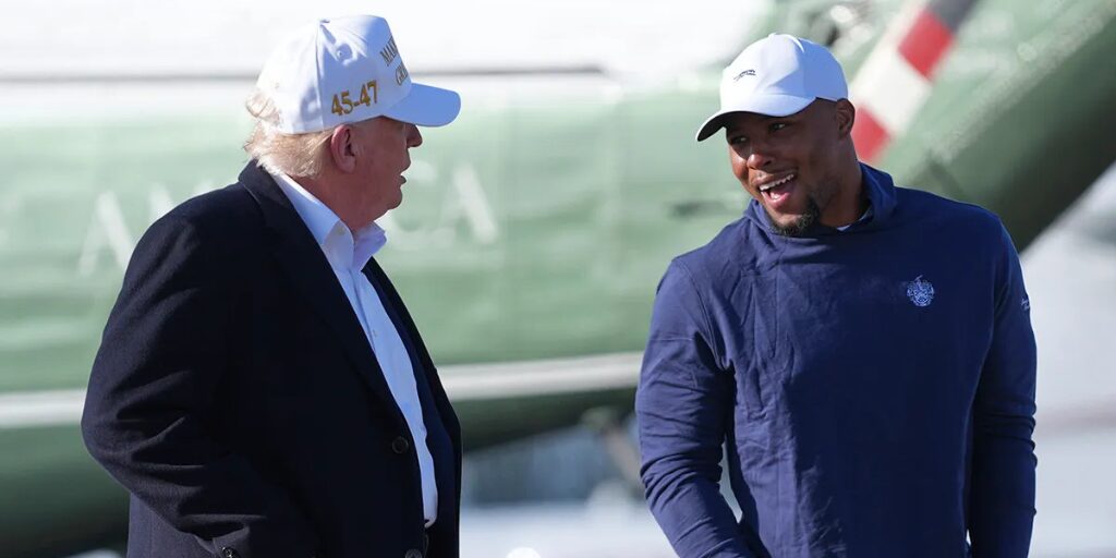 President Donald Trump and football player Saquon Barkley, wearing casual clothing and caps, talking and smiling outdoors.