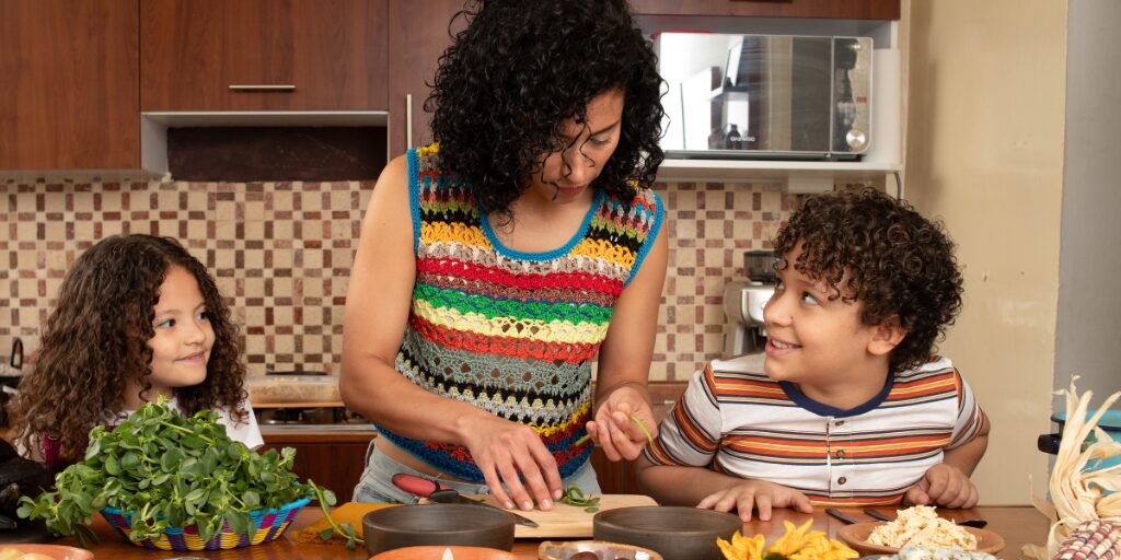 A woman cooks with two children in a cozy kitchen.