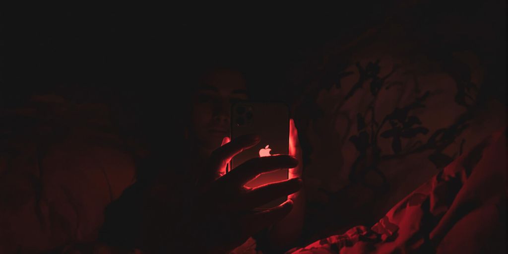Person using iPhone with red light in dark bedroom