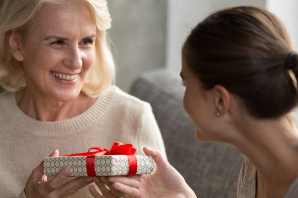Daughter giving a smiling older woman a gift wrapped with a red ribbon, capturing a heartfelt Mother's Day moment.
