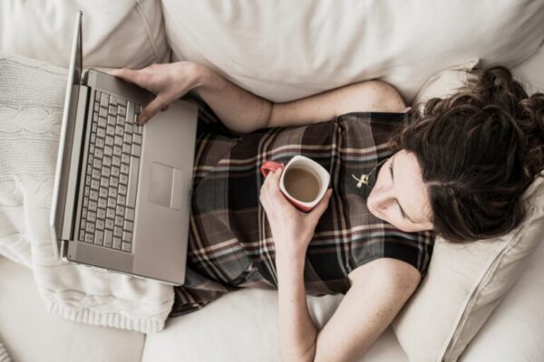 Woman relaxing on a couch with a laptop and a coffee mug, working comfortably in a cozy home setting