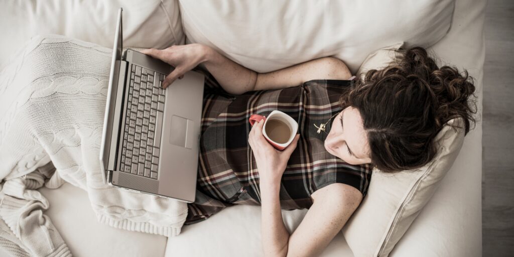 Woman relaxing on a couch with a laptop and a coffee mug, working comfortably in a cozy home setting
