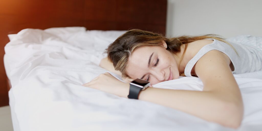 Woman peacefully sleeping on a bed, wearing a smartwatch.